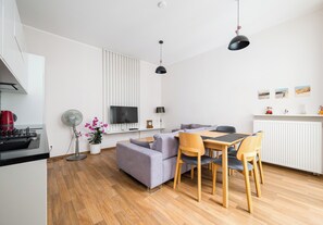 A modern kitchen with a built-in oven, a dining area with a table and chairs, a sofa, and a TV mounted on the wall. - Metro Politechnika Spacious Apartment (Warszawa)