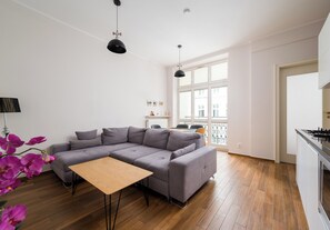 A modern living room with a grey sectional sofa, a wooden coffee table, and a dining area with a table and chairs. - Metro Politechnika Spacious Apartment (Warszawa)