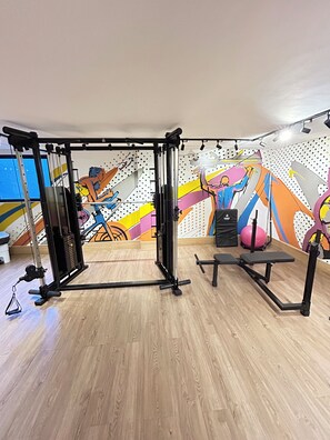 Een sportschool met een pull-up bar, een bankdrukrek en een kleurrijke muurschildering.