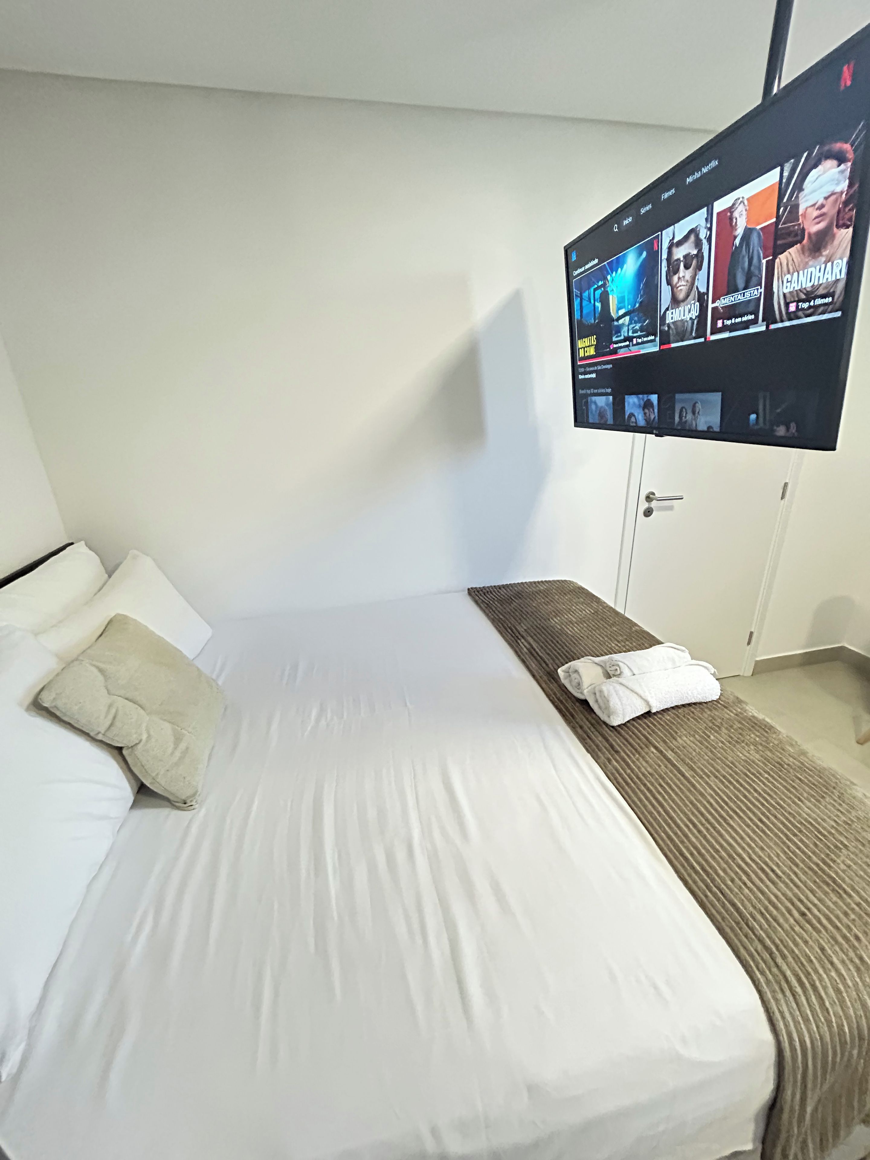 A hotel room with a bed, a TV mounted on the wall displaying a movie, and a door.