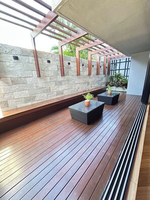 A covered outdoor area with wooden flooring, stone walls, and metal beams. - Melhores Flats - Prático, 30m do mar  (João Pessoa)