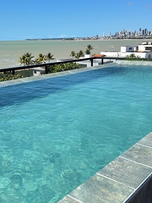 A clear pool with a city skyline in the background. - Melhores Flats - Prático, 30m do mar (João Pessoa)