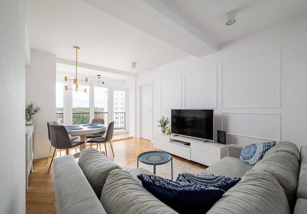 A modern living room with a sofa, TV, and dining area with chairs and a table. - Wola Spacious Signature Apartment (Warszawa)