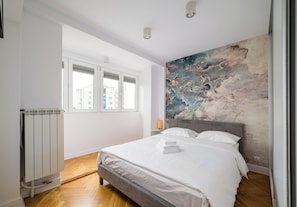 A bedroom with a bed, a radiator, a window, and a wall with a textured mural. - Wola Spacious Signature Apartment (Warszawa)