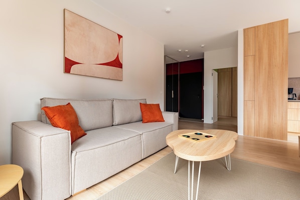 Uma sala de estar moderna com um sofá cinzento, duas almofadas laranja, uma mesa de centro de madeira e um grande quadro abstrato na parede.