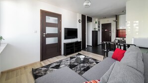 Un salon moderne avec un canapé, un téléviseur à écran plat, un coin repas et une cuisine en arrière-plan.