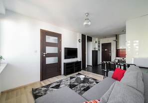A modern living room with a sofa, a flat-screen TV, a dining area, and a kitchen in the background. - Solec Powiśle Signature Apartment (Warszawa)