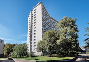 A modern high-rise building with a unique angular design, surrounded by a well-maintained park with trees and a paved walkway. - Solec Powiśle Signature Apartment (Warszawa)