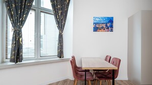 Ein Zimmer mit Esstisch, Stühlen, einem Fenster mit Vorhängen und einem Bild an der Wand.