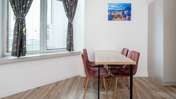 Une pièce comprenant une table à manger, des chaises, une fenêtre avec des rideaux et un tableau accroché au mur.