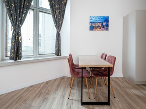 Una habitació amb taula de menjador, cadires, finestra amb cortines i un quadre a la paret.