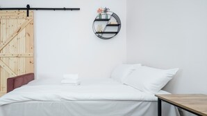 Ein schlicht eingerichtetes Schlafzimmer mit Bett, Holztür, runder Wandablage und kleinem Tisch.