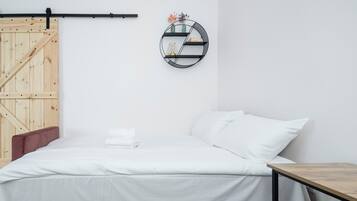 Une chambre à coucher au style minimaliste, avec un lit, une porte en bois, une étagère murale ronde et une petite table.