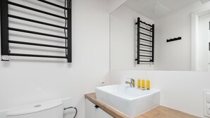 Ein modernes Badezimmer mit einem weißen Waschbecken, einer Holzauslage und einem schwarzen Handtuchhalter.