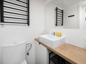 Un bany modern amb un lavabo blanc, tauleig de fusta i un penjador de tovalloles negre.