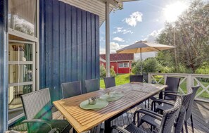 An outdoor patio with a wooden table and wicker chairs, a red building in the background, and a clear sky. - Nice home in Otterndorf with sauna (Otterndorf)