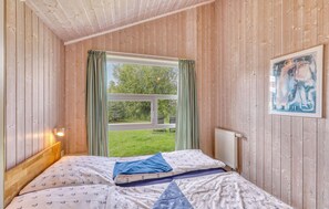 A room with wooden walls, a bed with patterned bedding, a window with curtains, and a painting on the wall. - Nice home in Otterndorf with sauna (Otterndorf)