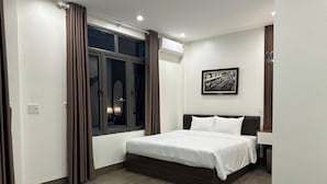 Ein Schlafzimmer mit einem Bett, einem Fenster mit Vorhängen, einer Wand-Klimaanlage und einem gerahmten Bild.