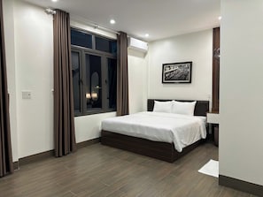 A bedroom with a bed, a window with curtains, a wall-mounted air conditioner, and a framed picture. - NESTA HOTEL  (Hoa Lu)