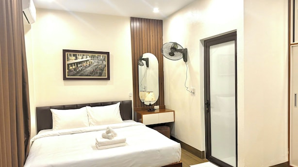 Ein Hotelzimmer mit einem Bett, einem Nachttisch mit Lampe, einem Wandventilator, einem gerahmten Bild und einer Schiebetür.