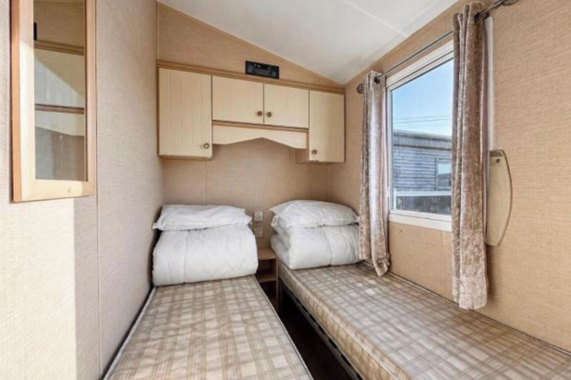 A compact room with two beds, a small cabinet, and a window with curtains.