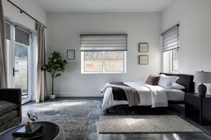 Une chambre à coucher moderne, avec un lit, des tables de chevet, une plante en pot et une vue sur l’extérieur.