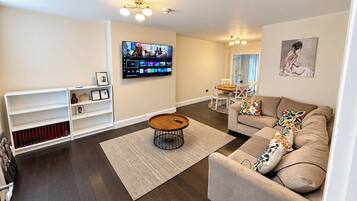 Una sala de estar moderna con un televisor de pantalla plana, una mesa redonda de centro, un sofá color beige y una estantería.
