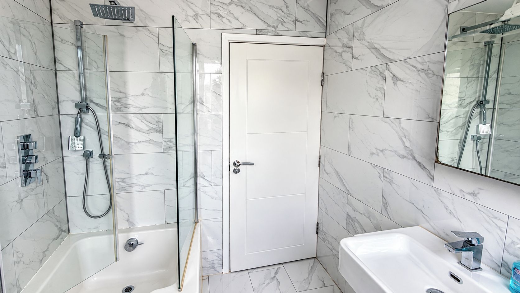 A bathroom with a glass-enclosed shower, a white door, and a white bathtub.