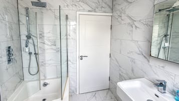 A bathroom with a glass-enclosed shower, a white door, and a white bathtub.
