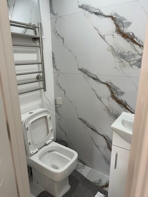 A modern bathroom with a toilet, a sink, and a marble backsplash. - Apartment Sleeps 2 with shared kitchen near city (London)