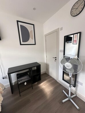 A room with a desk, a standing fan, a door, and a clock on the wall. - Apartment Sleeps 2 with shared kitchen near city (London)