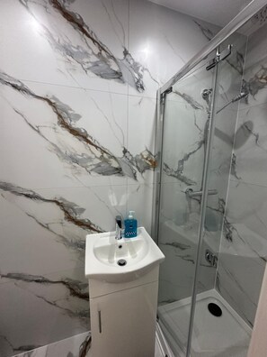 Ein Badezimmer mit Marmorwand, einem Waschbecken mit Seifenspender und einer Duschkabine aus Glas.