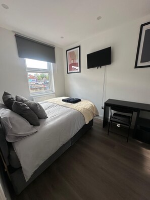 Ein Schlafzimmer mit Bett, Schreibtisch, Fernseher und Fenster mit Blick auf Gleise.