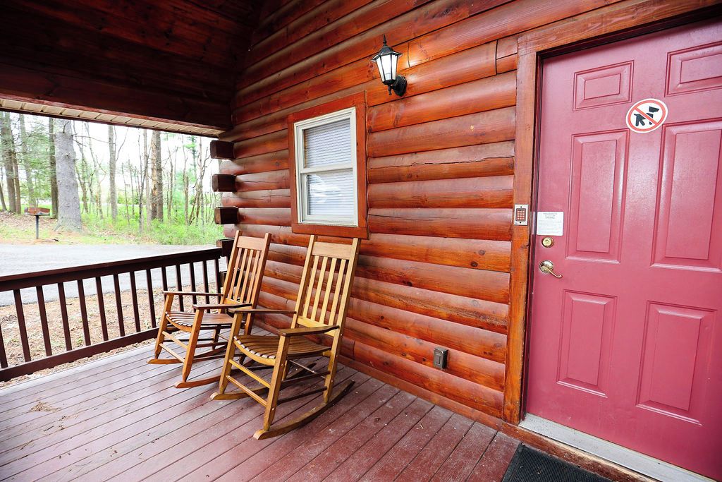 A wooden cabin with a red door, two rocking chairs on the porch, and a window with blinds.