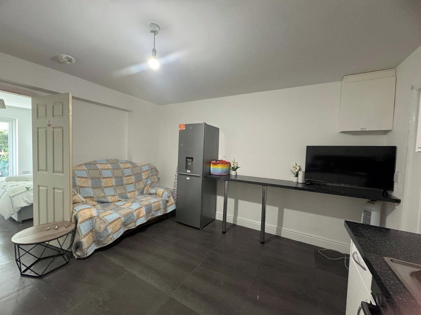 Ett kompakt bostadsutrymme med ett litet kök, en soffa, ett litet bord och en tv.