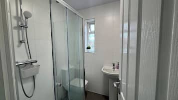Ett badrum med en dusch som är avskärmad med glasväggar, ett vitt handfat och en toalett.