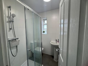 Ett badrum med en dusch som är avskärmad med glasväggar, ett vitt handfat och en toalett.