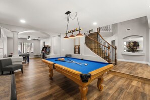 A spacious living room with a pool table, a staircase, and a large window. - Pool & Spa • Game Room • King Beds • 20 Guests Max (Las Vegas)