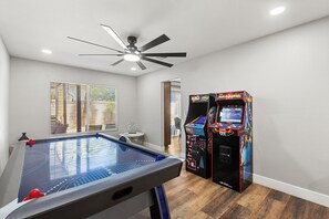 A pool table with a ceiling fan, two arcade machines, and a window with blinds. - Pool & Spa • Game Room • King Beds • 20 Guests Max (Las Vegas)
