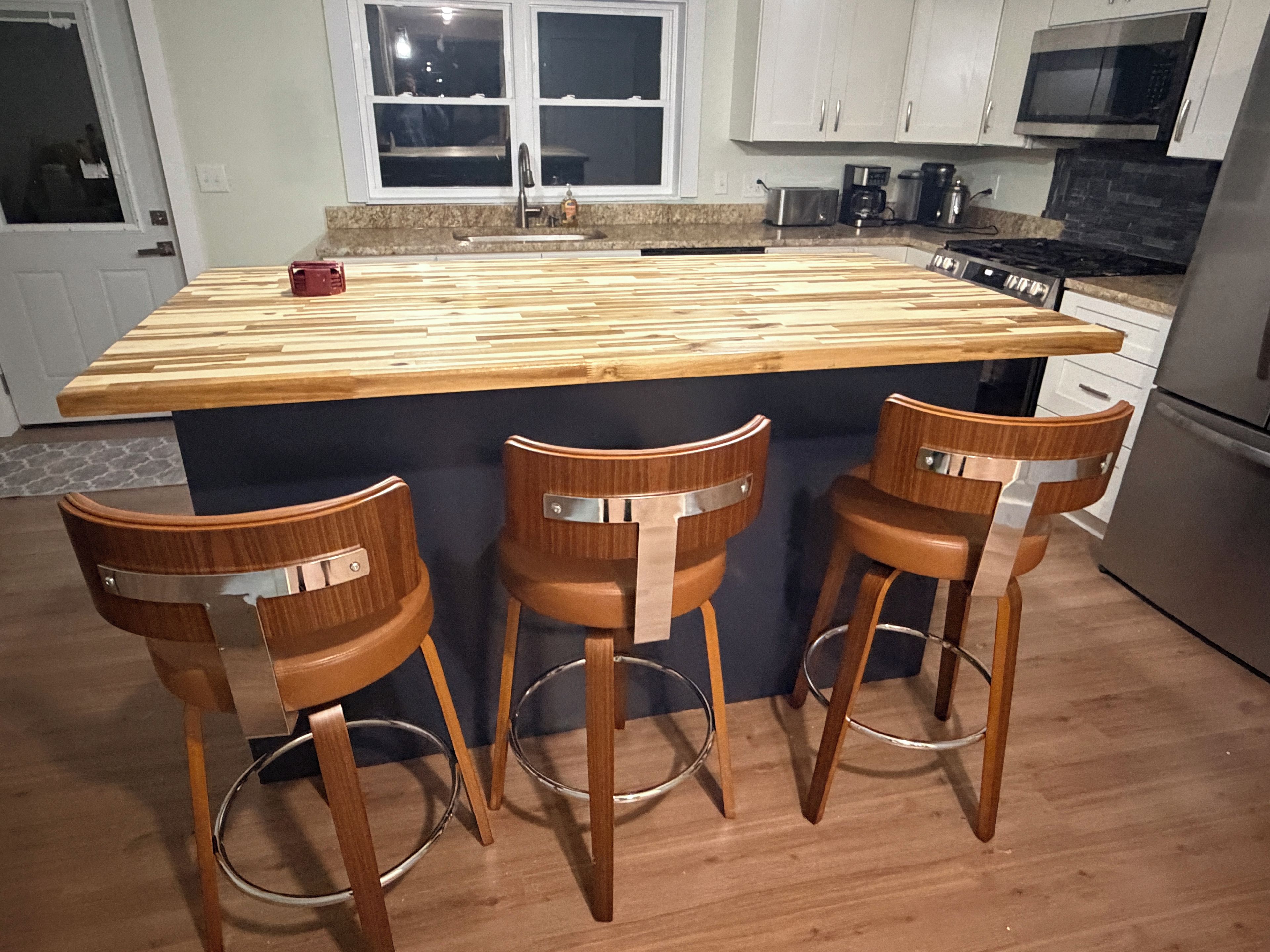 A kitchen with a wooden island, bar stools, stainless steel appliances, and a window above the sink.