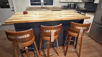 A kitchen with a wooden island, bar stools, stainless steel appliances, and a window above the sink.
