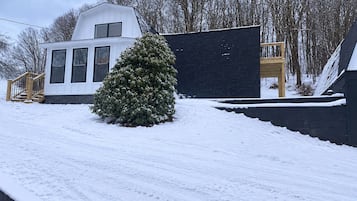 A snow-covered landscape with a white building, a black structure, and a coniferous tree.