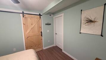 A bedroom with a bed, a wooden door, a white door, a ceiling fan, and a wall-mounted decoration.
