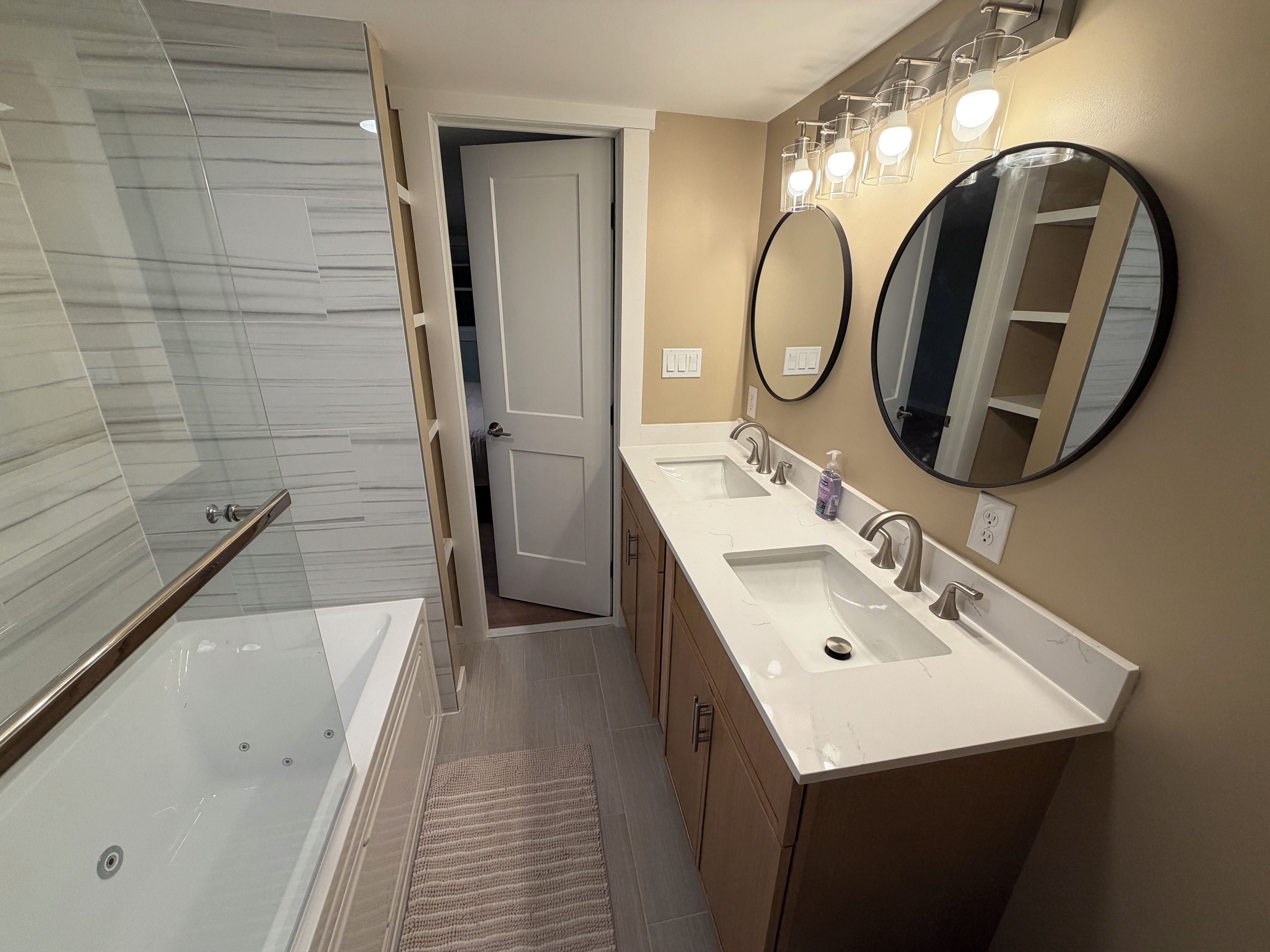 A modern bathroom with a glass shower enclosure, a walk-in shower, a double sink vanity, and two wall-mounted mirrors.