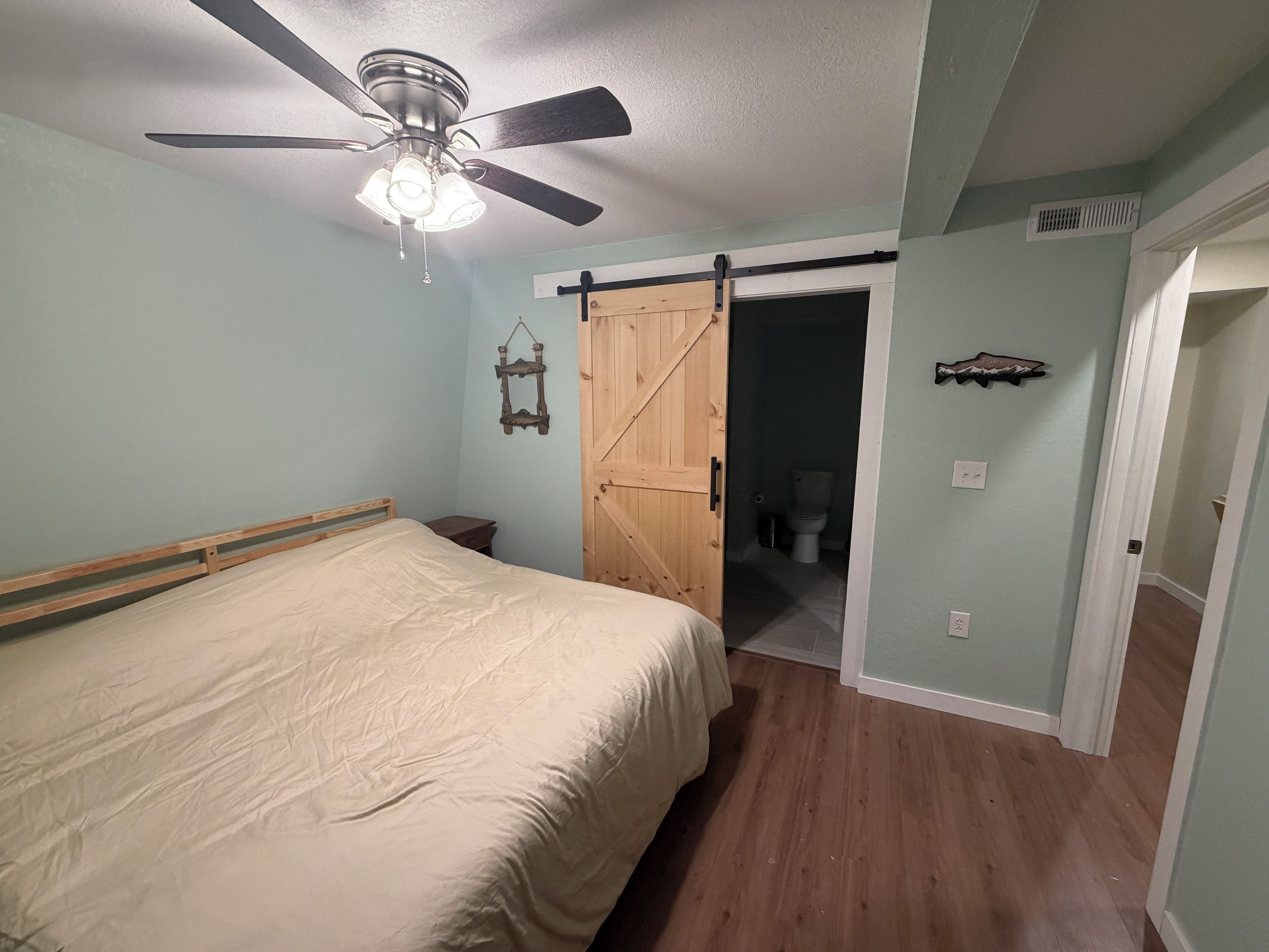 A bedroom with a bed, a ceiling fan, a wooden door, and a bathroom visible through an open door.