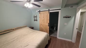A bedroom with a bed, a ceiling fan, a wooden door, and a bathroom visible through an open door.