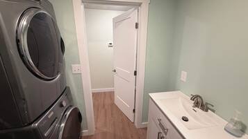 A laundry area with a front-loading washer and dryer, a white vanity with a sink, and a door leading to a hallway.