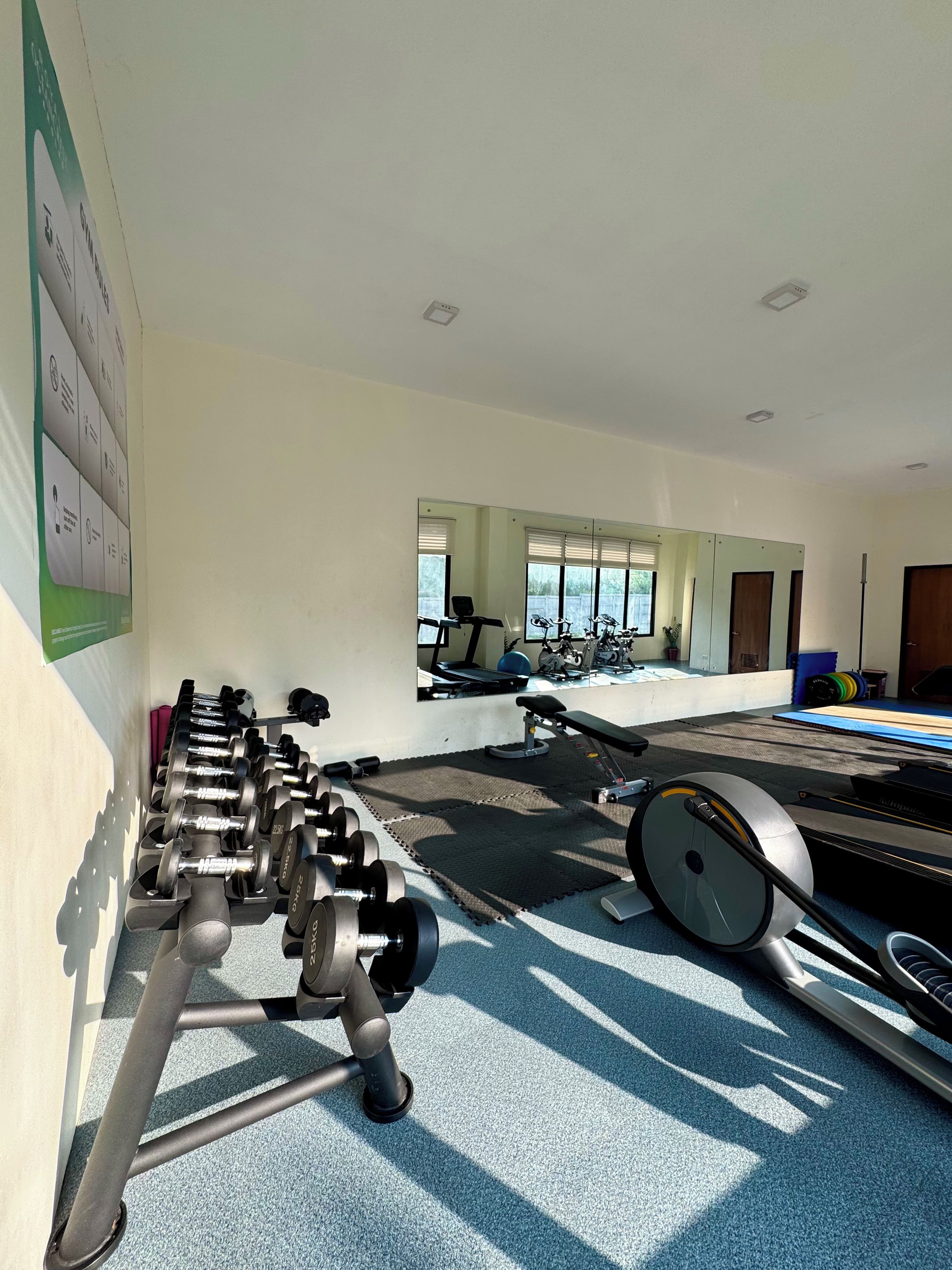 A gym with exercise equipment, a mirrored wall, and a window with blinds.