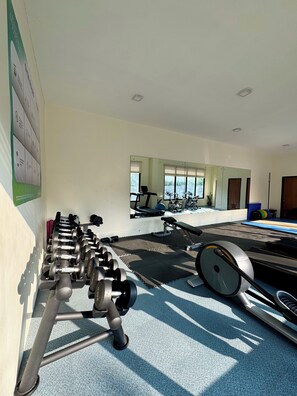 A gym with exercise equipment, a mirrored wall, and a window with blinds. - Royal Oceancrest Panglao 1 (Dauis)
