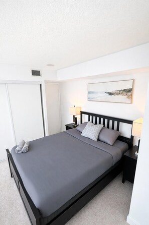 A neatly made bed with a grey mattress and pillows, a black headboard, and two bedside tables with lamps. - CityPlace Condo Suites near the Lake (Toronto)